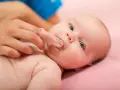 Delikatne czyszczenie dziąseł niemowlaka specjalną nakładką na palec, przygotowanie do pierwszego ząbka.