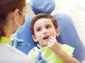 Chłopiec u dentysty, martwiący się o zbyt wczesne wypadanie zębów mlecznych.
