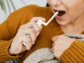 Kobieta aplikuje spray do gardła, by złagodzić ból i pieczenie spowodowane przez afty w gardle.