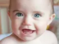 Uśmiechnięte niemowlę z niebieskimi oczami i dwoma ząbkami, radośnie pokazuje, kiedy wychodzą trójki.