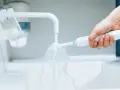 Ręka trzymająca szczoteczkę elektryczną pod bieżącą wodą z kranu. Prosty sposób, jak wyczyścić szczoteczkę elektryczną z kamienia.