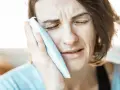 Kobieta z bólem zęba przykłada zimny okład. Może szuka naturalnych metod, jak szałwia na ból zęba.
