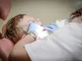 Chłopiec siedzi na fotelu dentystycznym podczas wizyty u dentysty. Dentysta w rękawiczkach bada jego zęby.
