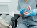 Dentysta w niebieskich rękawiczkach pokazuje na modelu, jak dbać o zęby, by uniknąć bólu dziąseł z tyłu.