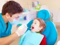Dentysta bada uśmiechniętego chłopca, sprawdzając, kiedy najpóźniej pierwszy ząbek pojawi się u malucha.