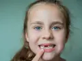 Uśmiechnięta dziewczynka z niebieskimi oczami pokazuje, kiedy wypadają jedynki górne.