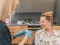 Dentystka w rękawiczkach przygotowuje preparat do fluoryzacji w ciąży. Uśmiechnięta pacjentka czeka na zabieg.