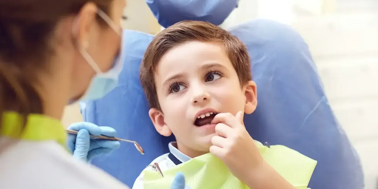 Chłopiec u dentysty, martwiący się o zbyt wczesne wypadanie zębów mlecznych.