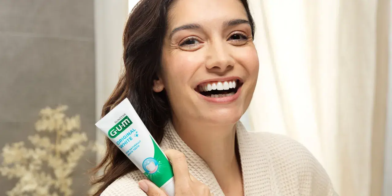 Uśmiechnięta kobieta trzymająca pastę GUM Original White. Dbanie o dziąsła (gum care) to klucz do pięknego uśmiechu.