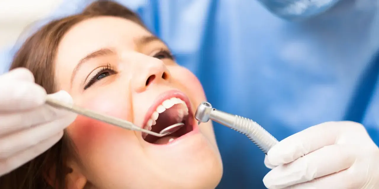 Pacjentka u dentysty, który bada jej usta. Widoczne narzędzia stomatologiczne i zaczerwienione dziąsło, sugerujące ropne zapalenie dziąseł.