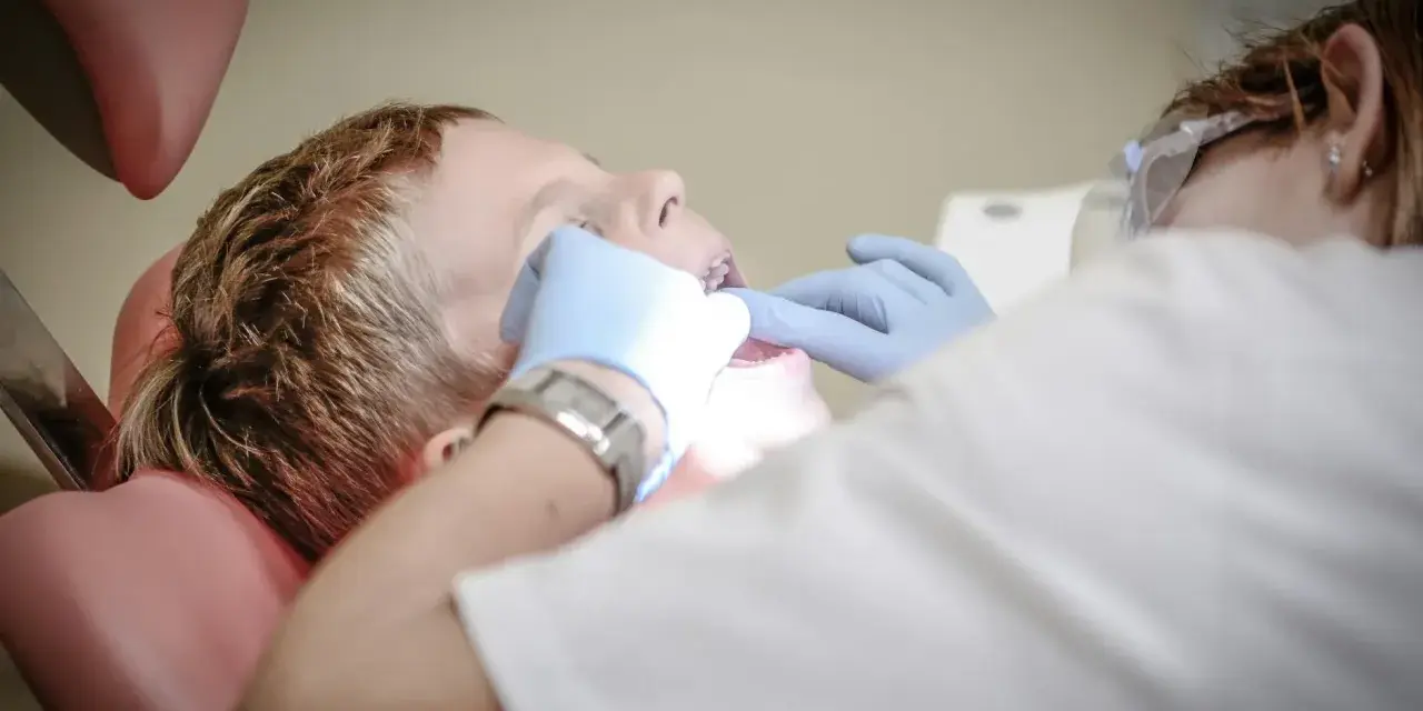 Chłopiec siedzi na fotelu dentystycznym podczas wizyty u dentysty. Dentysta w rękawiczkach bada jego zęby.