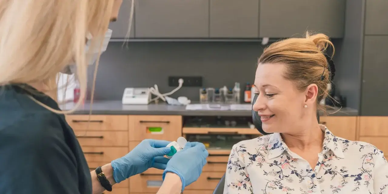 Dentystka w rękawiczkach przygotowuje preparat do fluoryzacji w ciąży. Uśmiechnięta pacjentka czeka na zabieg.