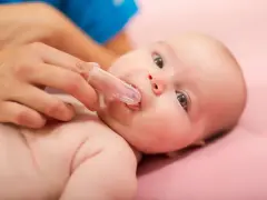 Delikatne czyszczenie dziąseł niemowlaka specjalną nakładką na palec, przygotowanie do pierwszego ząbka.