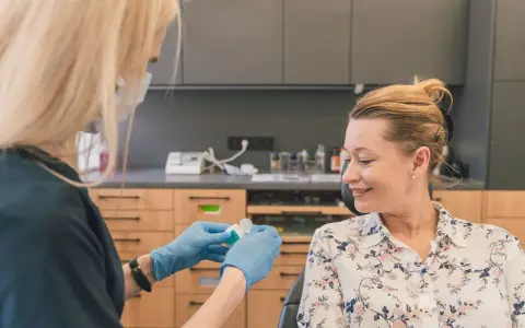Dentystka w rękawiczkach przygotowuje preparat do fluoryzacji w ciąży. Uśmiechnięta pacjentka czeka na zabieg.