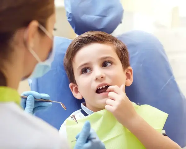 Chłopiec u dentysty, martwiący się o zbyt wczesne wypadanie zębów mlecznych.