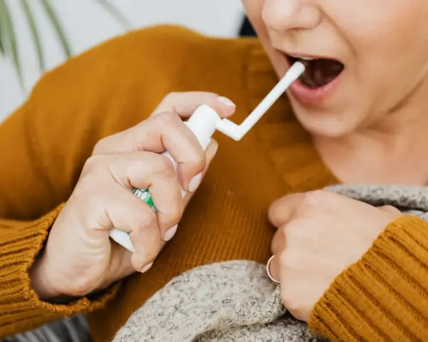 Kobieta aplikuje spray do gardła, by złagodzić ból i pieczenie spowodowane przez afty w gardle.