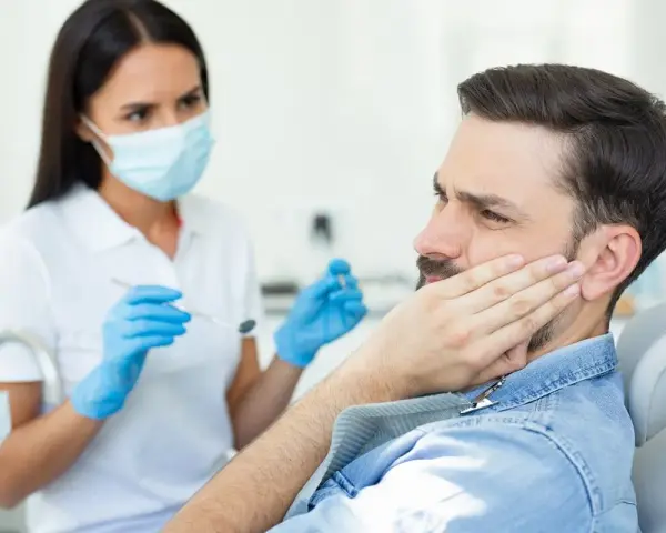 Mężczyzna z bólem policzka u dentysty, który bada jego dziąsła. Może to być objaw problemów z kieszonkami dziąsłowymi.