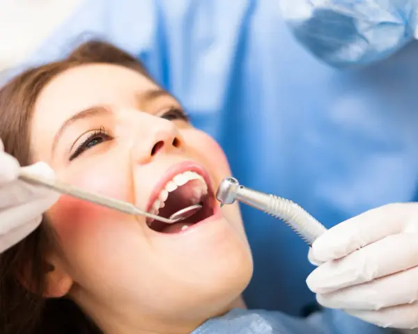 Pacjentka u dentysty, który bada jej usta. Widoczne narzędzia stomatologiczne i zaczerwienione dziąsło, sugerujące ropne zapalenie dziąseł.