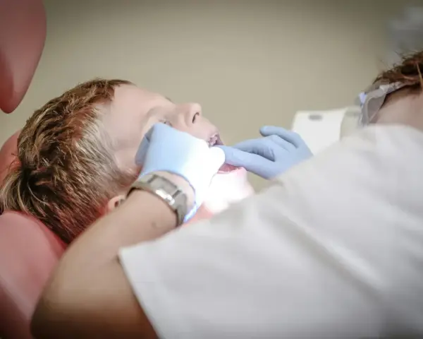 Chłopiec siedzi na fotelu dentystycznym podczas wizyty u dentysty. Dentysta w rękawiczkach bada jego zęby.