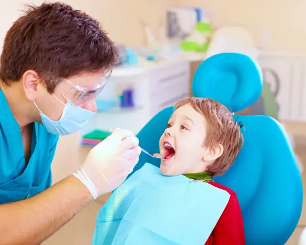 Dentysta bada uśmiechniętego chłopca, sprawdzając, kiedy najpóźniej pierwszy ząbek pojawi się u malucha.
