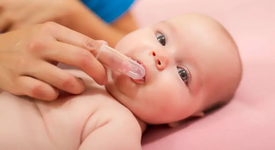 Delikatne czyszczenie dziąseł niemowlaka specjalną nakładką na palec, przygotowanie do pierwszego ząbka.