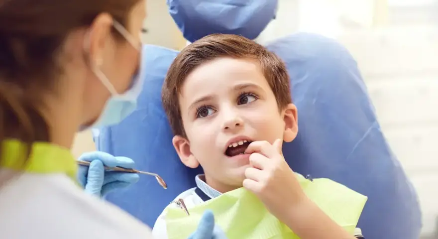 Chłopiec u dentysty, martwiący się o zbyt wczesne wypadanie zębów mlecznych.