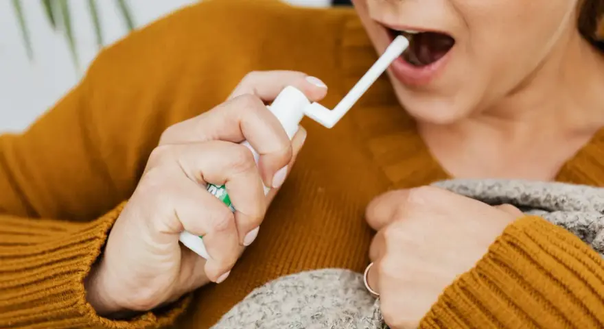 Kobieta aplikuje spray do gardła, by złagodzić ból i pieczenie spowodowane przez afty w gardle.