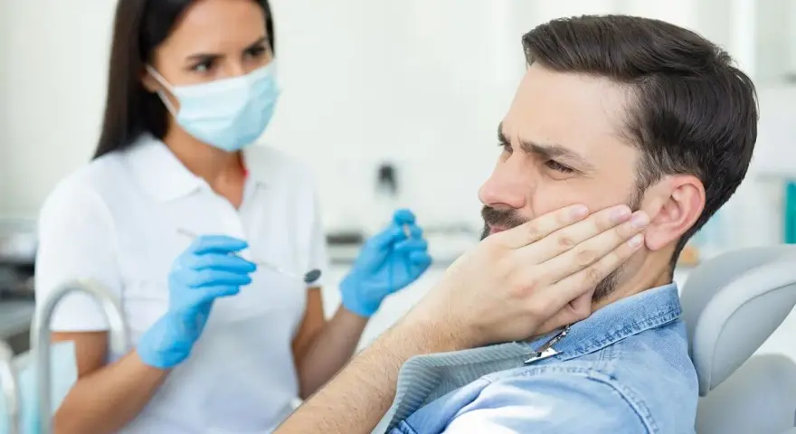 Mężczyzna z bólem policzka u dentysty, który bada jego dziąsła. Może to być objaw problemów z kieszonkami dziąsłowymi.