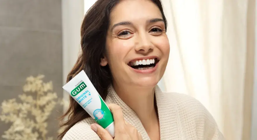 Uśmiechnięta kobieta trzymająca pastę GUM Original White. Dbanie o dziąsła (gum care) to klucz do pięknego uśmiechu.