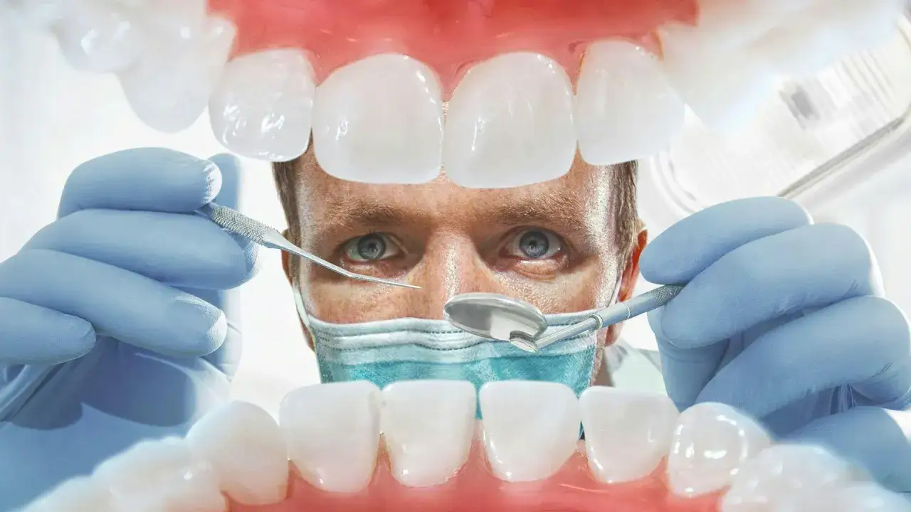 Dentysta w rękawiczkach bada zęby pacjenta. Widok z jamy ustnej, gdzie widać białe zęby i różowe, pulsujące dziąsła.