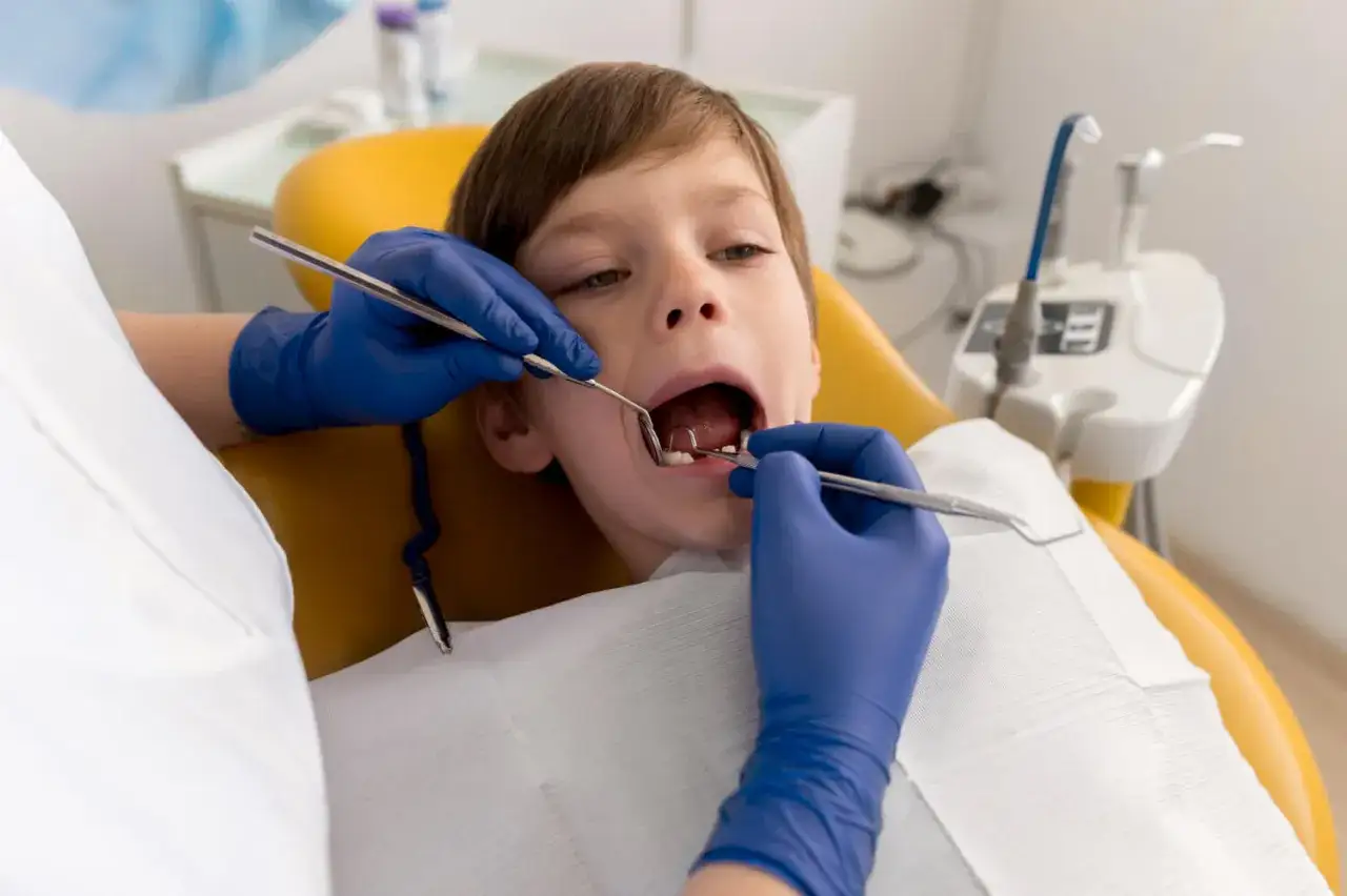 Chłopiec u dentysty. Lekarz bada jego zęby, sprawdzając, jak długo rusza się mleczak zanim wypadnie.