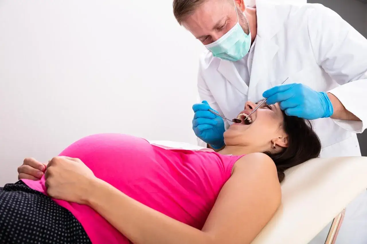 Dentysta bada zęby ciężarnej kobiety. Dbałość o higienę jamy ustnej, w tym fluoryzacja w ciąży, jest ważna dla zdrowia przyszłej mamy i dziecka.
