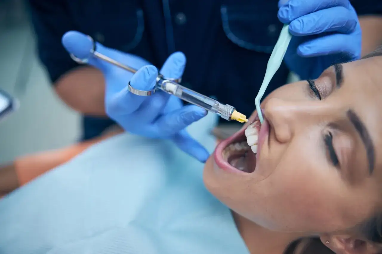 Dentysta podaje znieczulenie miejscowe pacjentce, która otwiera usta.