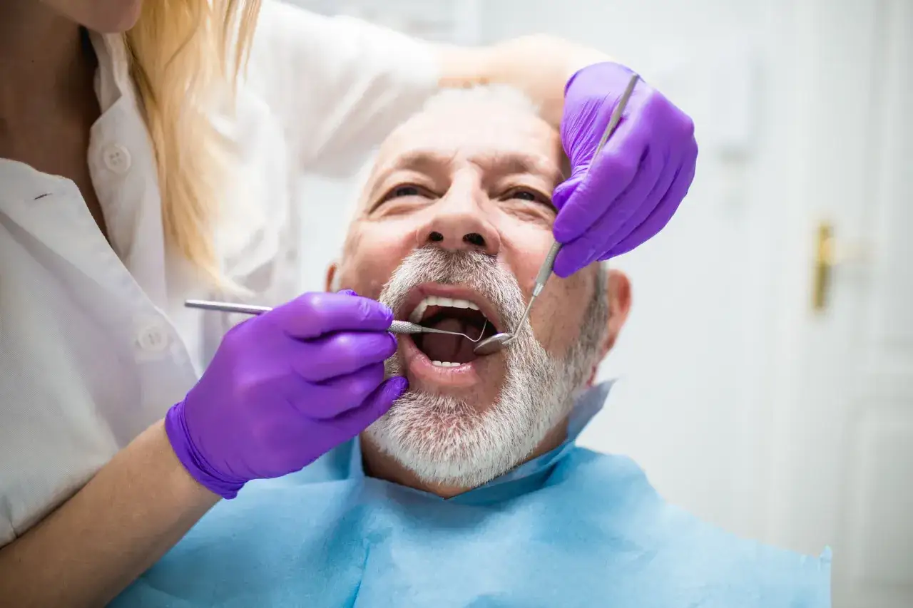 Dentysta bada uśmiech starszego mężczyzny, sprawdzając, czy dziąsło nachodzące na ząb nie stanowi problemu.