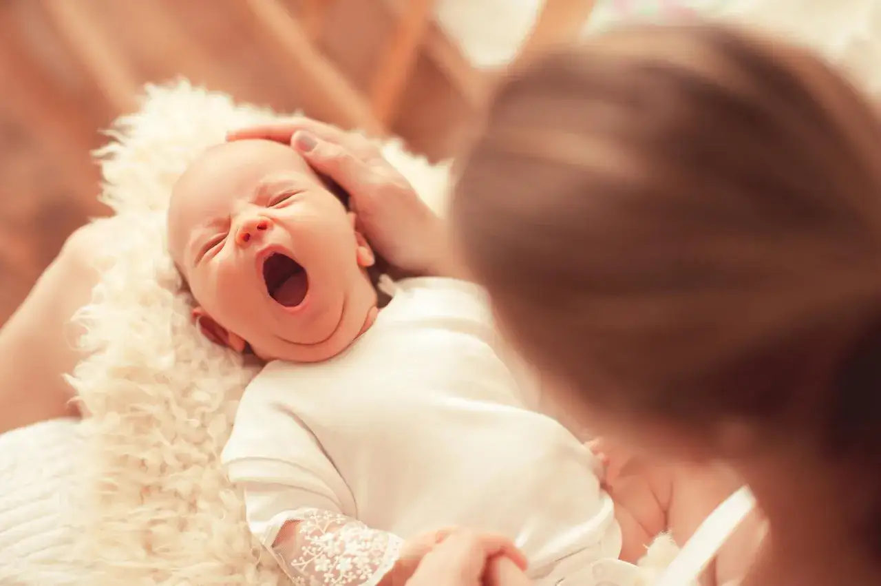 Malutkie ząbki u noworodka, który ziewa. Mama delikatnie głaszcze główkę dziecka.