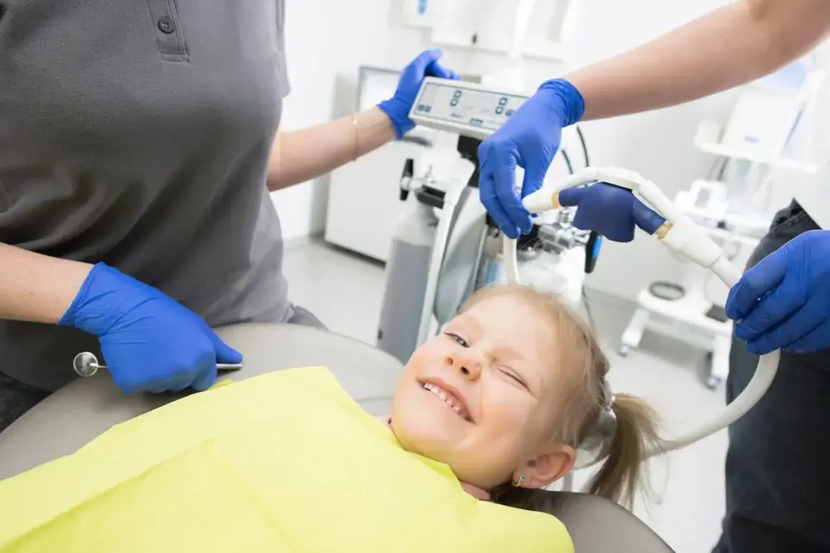 Uśmiechnięta dziewczynka u dentysty. Zastanawia się, ile czasu rośnie ząb stały, podczas gdy personel medyczny przygotowuje sprzęt.