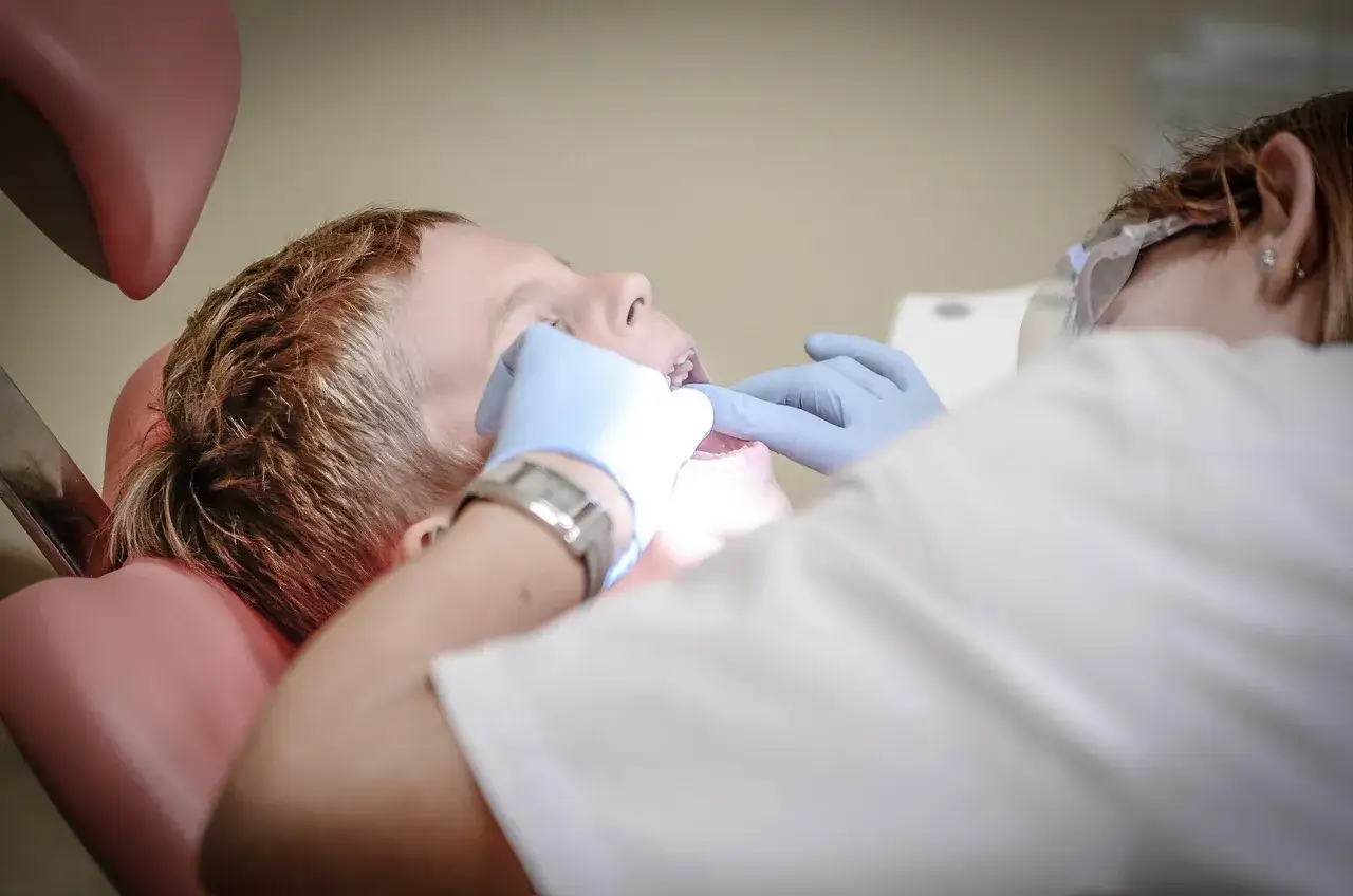 Dentysta bada zęby chłopca, szukając rozwiązania, czym płukać stan zapalny zęba.